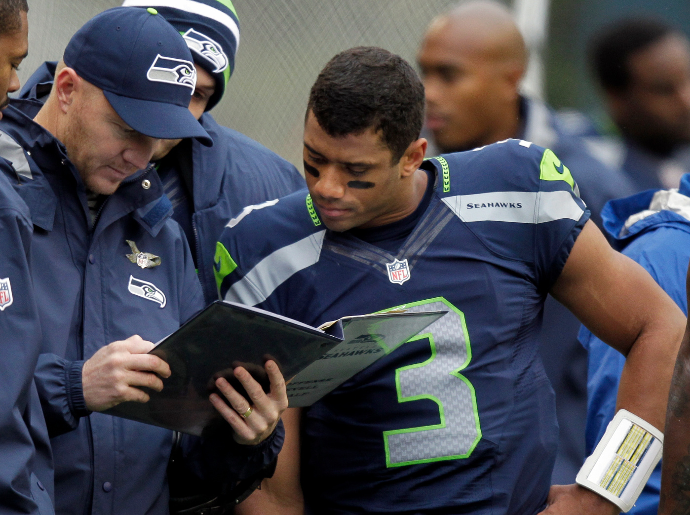 FILE - In this Nov. 11, 2012, file photo, Seattle Seahawks quarterback Russell Wilson, right, looks at a playbook with offensive coordinator Darrell Bevell, left, on the sidelines during the first half of an NFL football game against the New York Jets in Seattle. Even though Wilson will play his first playoff game Sunday at Washington, Bevell expects more of the same poise he's seen out of his QB all season. (AP Photo/Stephen Brashear, File)